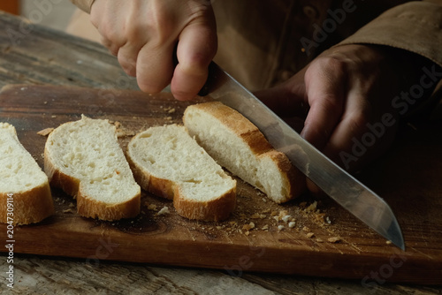 Hands slicing freshly baked loaf of ciabatta bread on wooden cutting board.