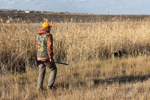 Mature man hunter with gun while walking on field.