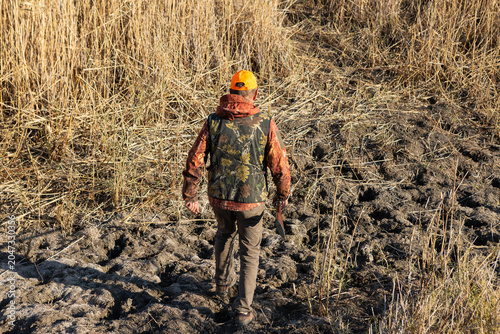 Mature man hunter with gun while walking on field.