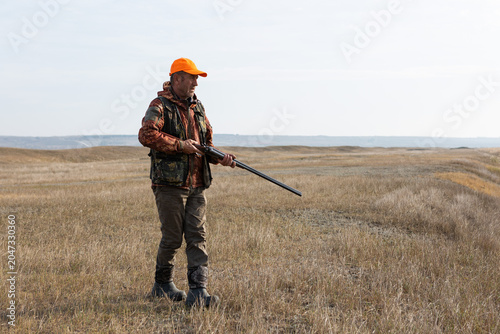Mature man hunter with gun while walking on field.