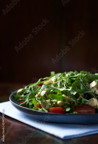Green salad with feta cheese, olives and arugula leaves. Rustic wooden background. Soft focus.