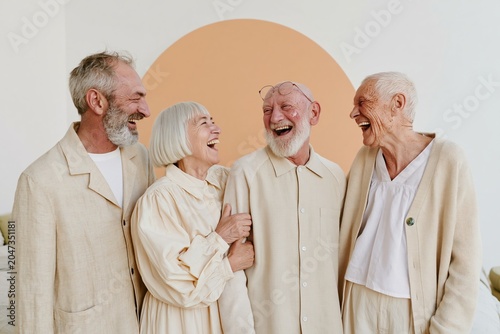 Group of senior friends standing together and laughing in a bright room for senior wellness, retirement lifestyle and community healthcare advertising