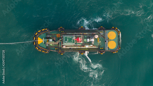 Aerial view of a tugboat navigating through green sea water with white wake and towing line in Laem Chabang, Chon Buri, Thailand.