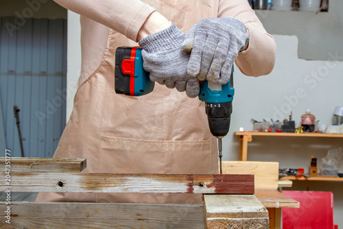 Foto Woman carpenter using a cordless drill to drive a screw into a wooden plank