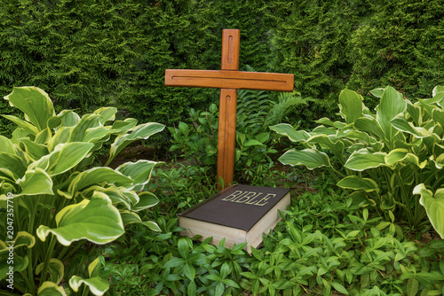 Bible and wooden cross on the meadow. Christian concept of faith in God, divine truth, and the redemptive grace of Jesus