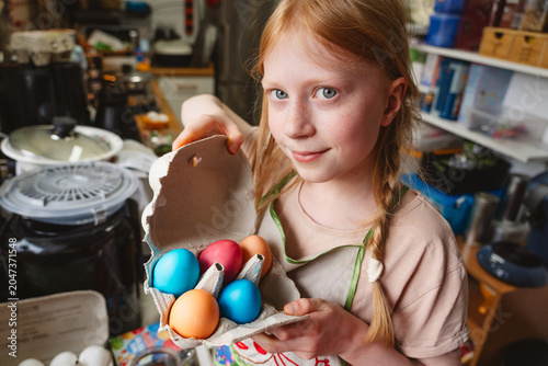 Girl holding carton of colorful Easter eggs in the kitchen