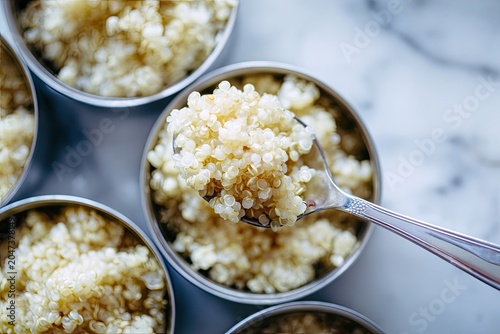 Close-up of fluffy cooked quinoa being portioned from a bowl with a silver spoon