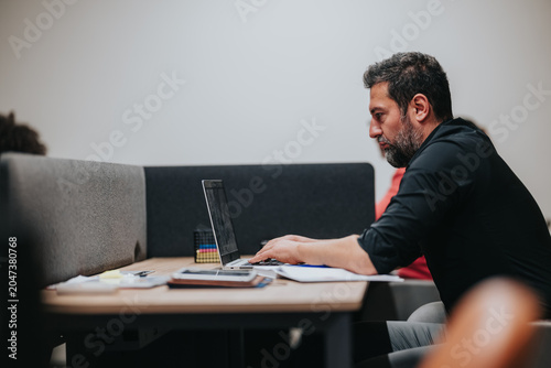 Foto A focused businessman types on a laptop while seated at a shared office desk