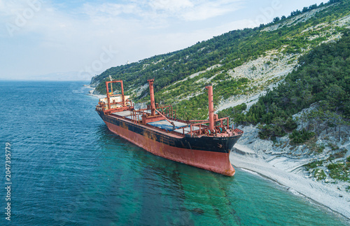 Fotografie Grounded derelict cargo ship on a rocky Black Sea beach with green mountains und