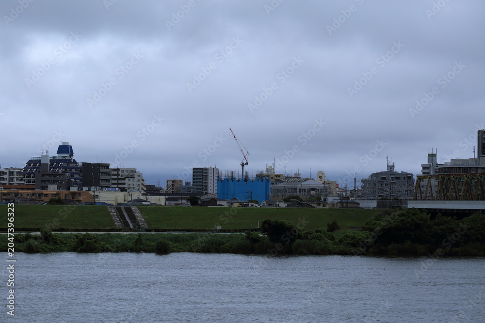 Fototapeta premium 台風通過後の雨雲 暴風雨後の河川と都市風景 / Heavy overcast sky over a river and city buildings after a tropical typhoon
