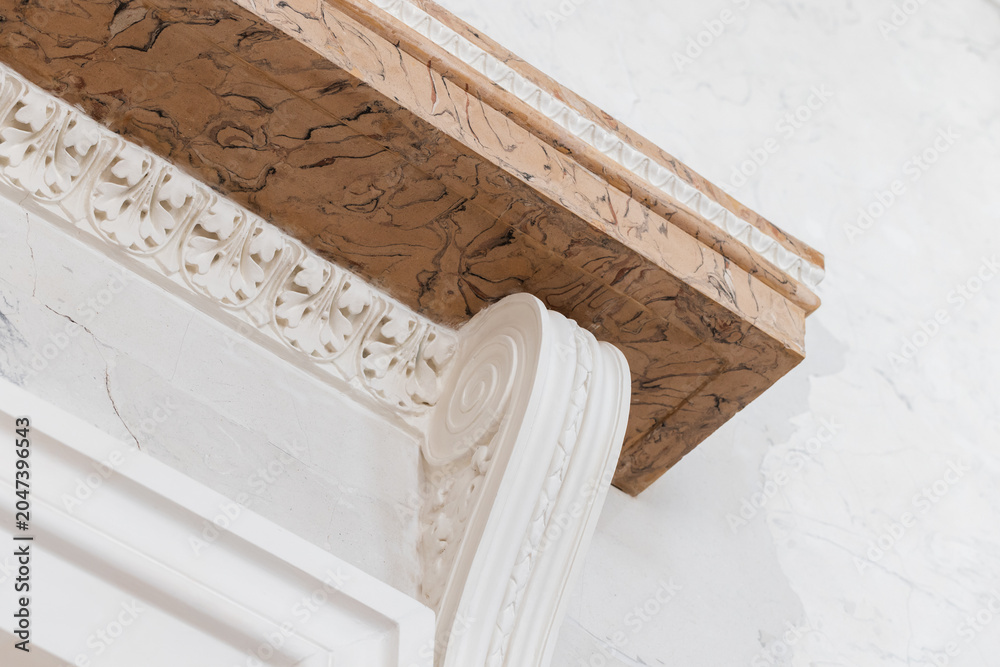 Fototapeta premium Close-up of an ornate marble cornice and decorative plaster column showcasing classical scrollwork, carved acanthus motifs and textured molding in a bright historic interior space