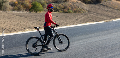 Cyclist riding bicycle on road against clear sky. A man in an outfit stands with a bicycle on an autumn sunny day.