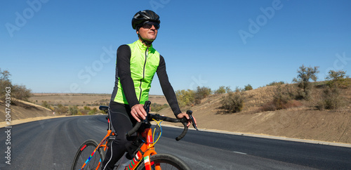 Cyclist riding bicycle on road against clear sky. A man in an outfit stands with a bicycle on an autumn sunny day.