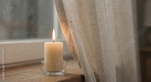 Lit candle burning dangerously close to linen curtain near window fire hazard and home safety concept