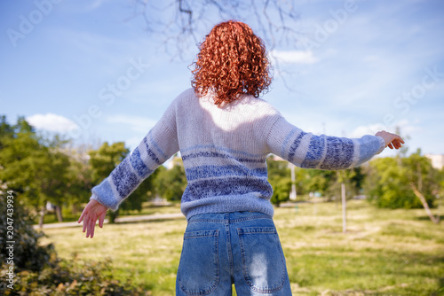Young woman with curly red hair dancing back to camera on green natural background. Reducing stress and anxiety. Connection with nature. Physical movement, dance, mental health