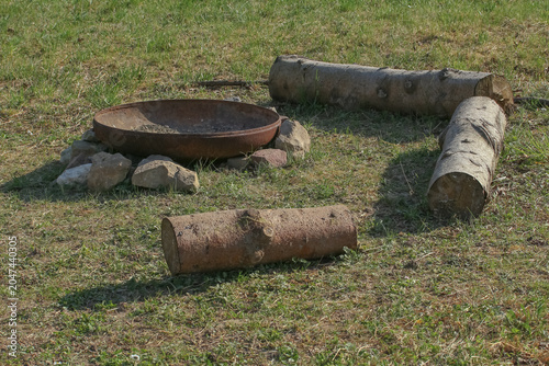 Grillplatz auf einer Wiese mit Baumstämmen zum Sitzen und einer Feuerschale