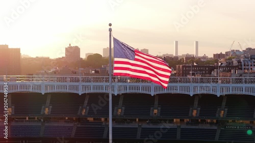 American flag waving in wind with New York City South Bronx skyline, revealing empty Yankee Stadium seats and facade during warm and hazy sunset