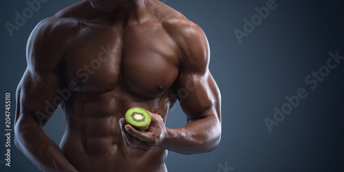 Muscular man holds kiwi fruit, showcasing strength and health in dramatic lighting setting