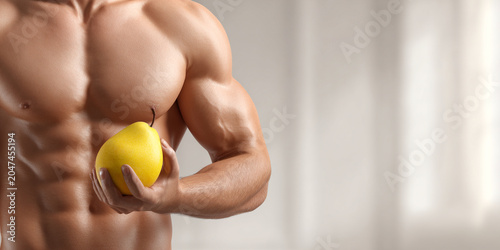 Muscular man holds yellow pear, showcasing strength and health in bright, minimalistic setting