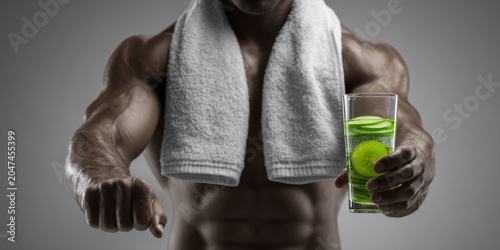 Refreshing drink with cucumber slices held by muscular man after workout, showcasing fitness and hydration
