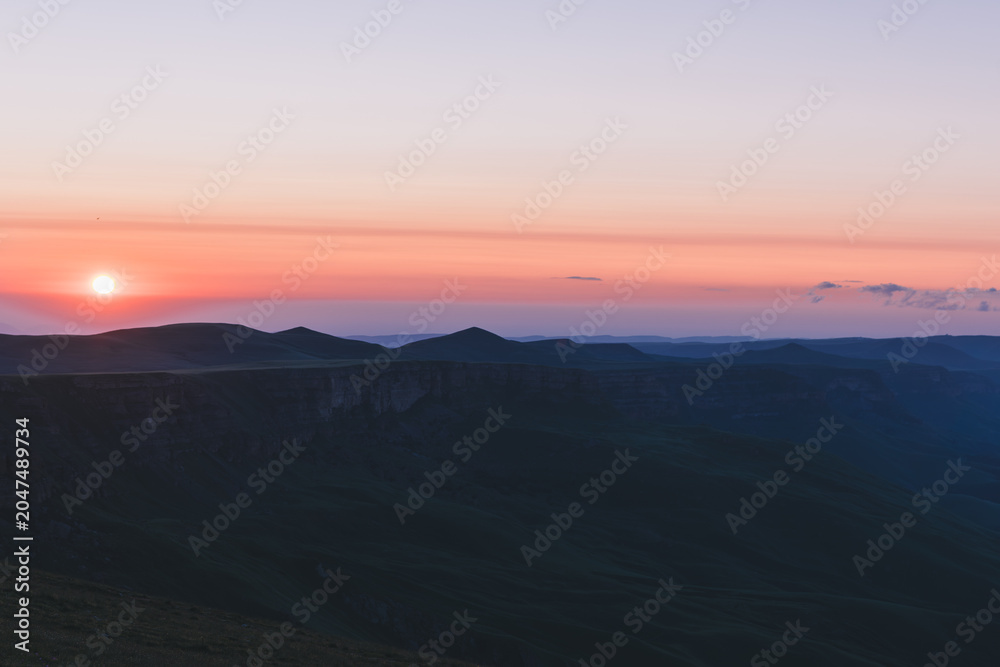 Obraz premium Wide landscape view of sunrise over Bermamyt Plateau, Karachay-Cherkess Republic, Russia, with dark mountain silhouettes, soft clouds, and colorful dawn sky