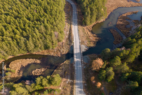 Top down aerial view of a paved road bridge crossing a winding river and wetlands, surrounded by mixed forest in Sverdlovsk Oblast, Russia, autumn landscape
