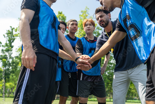 фотографія Diverse group of young soccer players stacking hands with coach before football match outdoor