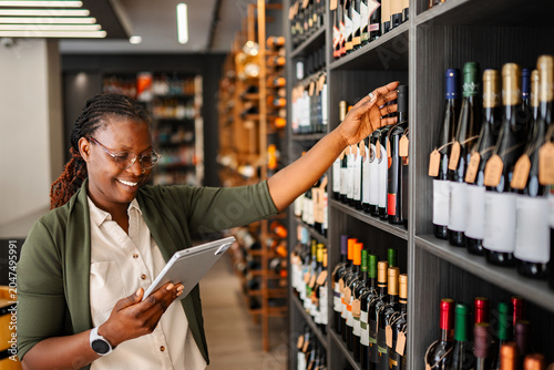 Fotografija African American woman managing wine store inventory with digital tablet