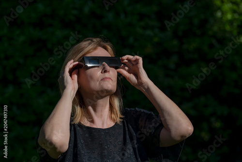 A woman wears special black glasses to observe the sun during a solar eclipse