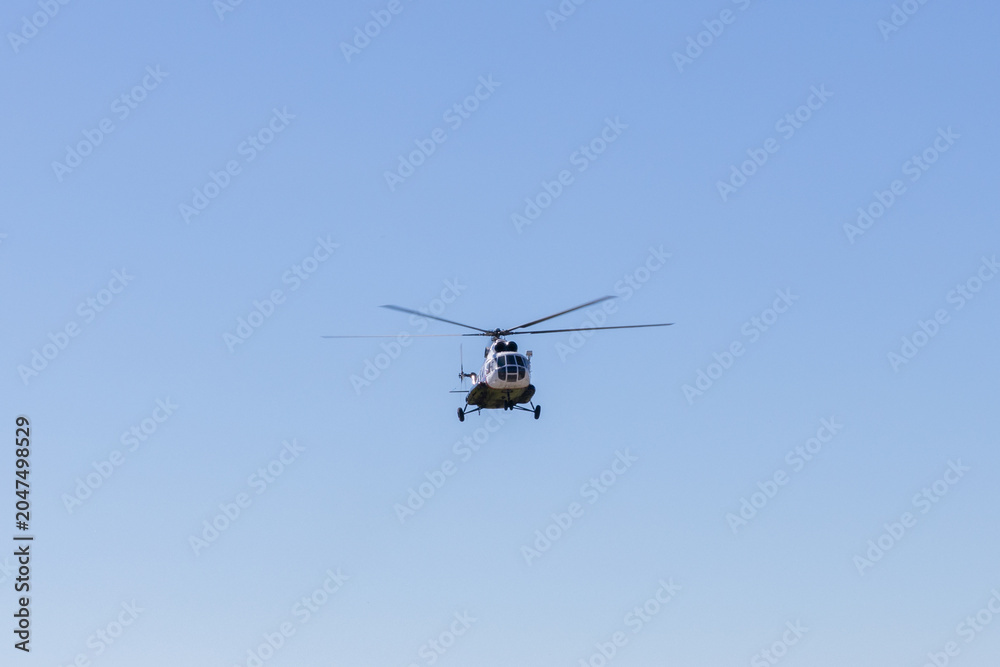 Fototapeta premium Front view of a helicopter flying high against a clear blue sky with wide copy space, ideal for aviation, transport, rescue, security, and travel concepts