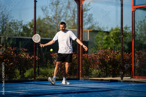 Foto Man playing padel on blue court hitting ball