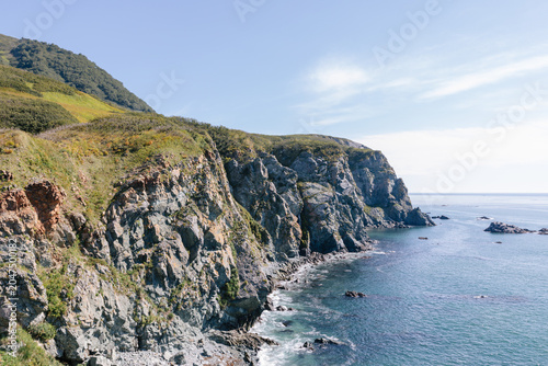 Schilderij op canvas Scenic rocky shoreline with steep sea cliffs, green tundra hills and calm blue w