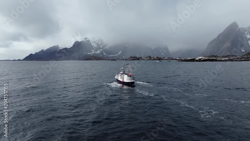 Fishing boat sailing toward rocky misty shoreline under overcast skies