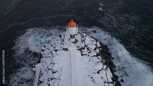 Small White Lighthouse with Orange Roof on Snowy Rocky Jetty in Winter Sea