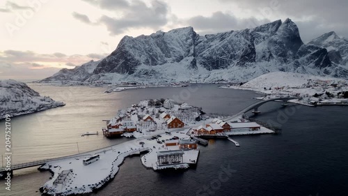 Aerial view of snow-covered coastal village on island with curved bridge and jagged mountains