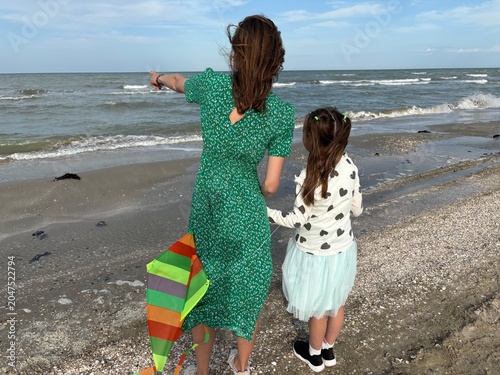 Schilderij op canvas a mother and daughter standing on a sandy and pebbly beach with their backs to the camera