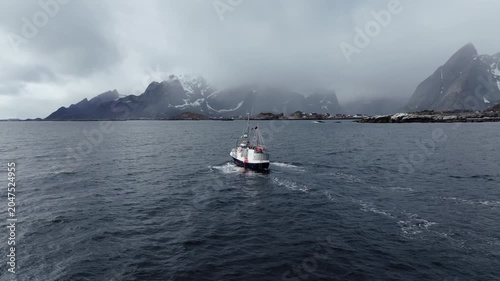 Fishing boat crossing choppy sea toward foggy mountainous coastline with coastal village