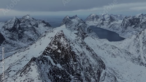 Aerial view of jagged snow-covered mountain summit above a fjord-like lake