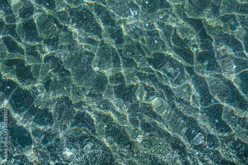 Fotografía Clear turquoise ocean water ripples with sunlight reflections over sandy sea flo