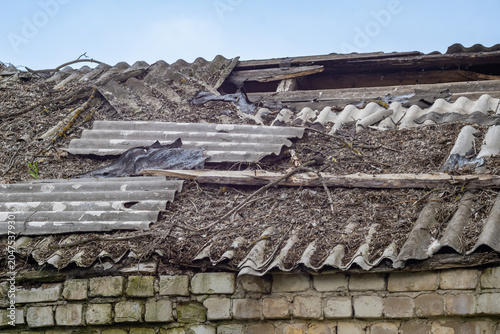 Photos Damaged slate roof of an old brick building, close-up against a blue sky, conce