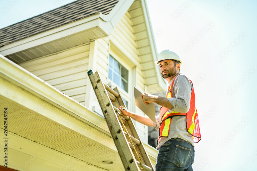 Fototapeta premium Man with a white hard hat holding a clipboard, inspect house