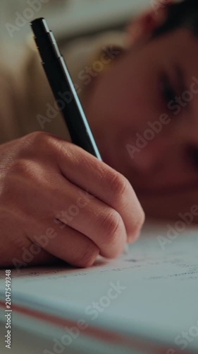 Close-up of a student's hand writing with a pen in a notebook. A focused person doing homework or studying. Vertical video.