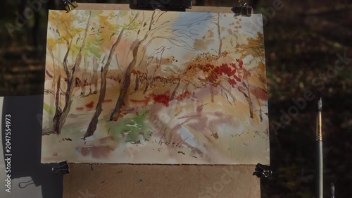 Autumn landscape painted in watercolor on an artist's easel in the forest on a sunny day