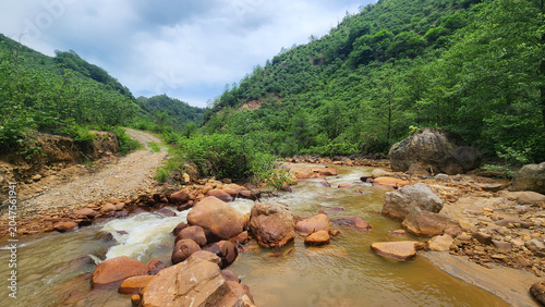Bilde på lerret A stream colored red-orange by mining pollution, showing acid mine drainage effects where dissolved metals oxidize and form iron-rich sediments in the water and riverbed