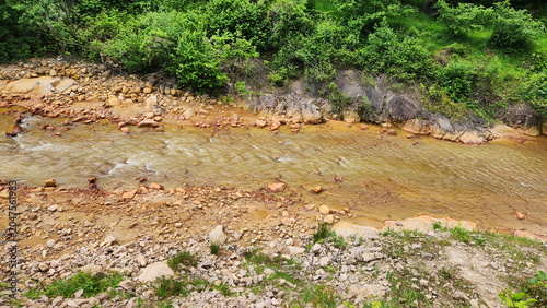 A stream colored red-orange by mining pollution, showing acid mine drainage effects where dissolved metals oxidize and form iron-rich sediments in the water and riverbed.