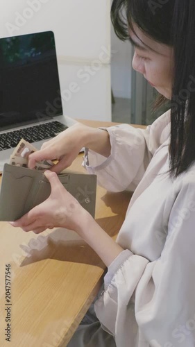 Asian woman taking banknotes out of wallet at table