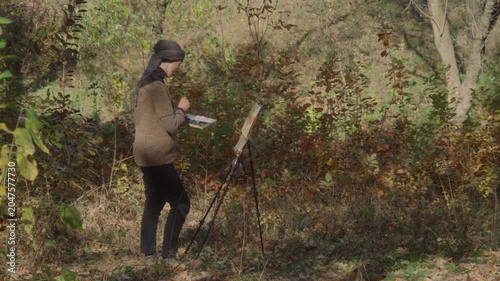 Artist mixing watercolor palette while standing in front of easel in autumn forest