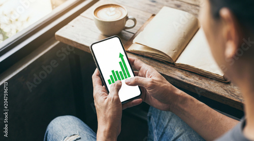Close up person holding smartphone with rising green chart