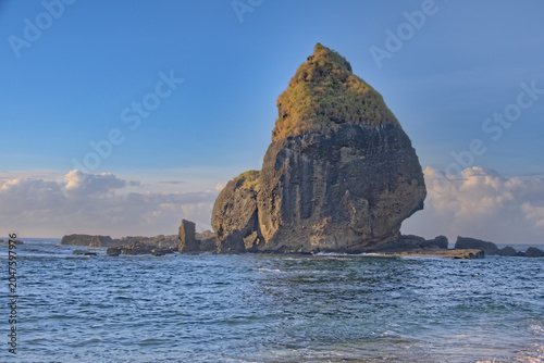 Foto Towering volcanic sea stack rock with a pointed peak rising dramatically from ocean waters under a clear blue sky