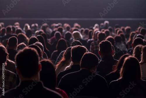 Konstfotografi Large seated audience watching performance in dim auditorium, silhouettes and backlit heads create quiet, focused atmosphere